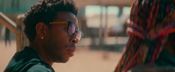 Movie still from “End of the Road” (2022), directed by Millicent Shelton – A person wearing glasses; Close Up shot, Over the shoulder angle