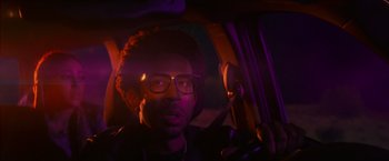 Movie still from “End of the Road” (2022), directed by Millicent Shelton – A man with glasses sitting in the driver's seat of a car; Close Up shot, Over the shoulder angle