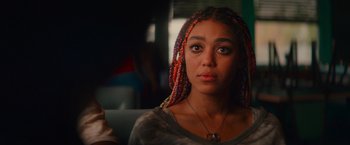 Movie still from “End of the Road” (2022), directed by Millicent Shelton – A woman with colorful braids sitting on a couch; Close Up shot, Over the shoulder angle