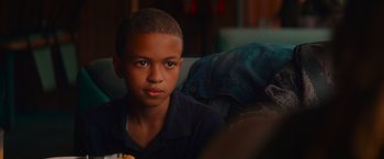 Movie still from “End of the Road” (2022), directed by Millicent Shelton – A young boy sitting on a couch looking at the camera; Close Up shot, Over the shoulder angle