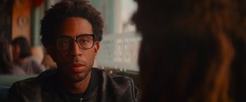 Movie still from “End of the Road” (2022), directed by Millicent Shelton – A person wearing glasses and a leather jacket; Close Up shot, Over the shoulder angle