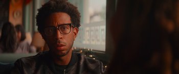 Movie still from “End of the Road” (2022), directed by Millicent Shelton – A person wearing glasses and a jacket; Close Up shot, Over the shoulder angle