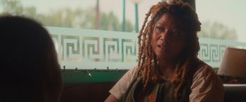 Movie still from “End of the Road” (2022), directed by Millicent Shelton – A woman with dreads sitting at a table in front of a window; Close Up shot, Over the shoulder angle
