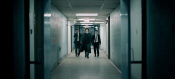 Three men in suits are walking down a hall way