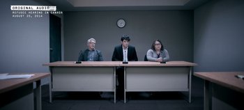 A group of people sitting at a long table in front of a wall clock