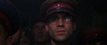 Movie still from “Enemy at the Gates” (2001), directed by Jean-Jacques Annaud – A man wearing a hat and glasses with another man standing behind him; Close Up shot, Low angle