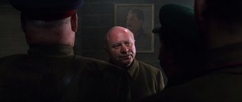 Movie still from “Enemy at the Gates” (2001), directed by Jean-Jacques Annaud – A man in a military uniform standing in front of a painting of mao zedong; Close Up shot, Over the shoulder angle