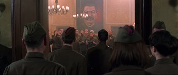 Movie still from “Enemy at the Gates” (2001), directed by Jean-Jacques Annaud – A group of men in military uniforms standing in front of a painting of stalin; Wide shot, Low angle