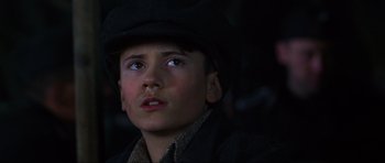 Movie still from “Enemy at the Gates” (2001), directed by Jean-Jacques Annaud – A young boy wearing a black hat looking up at the sky; Close Up shot, Low angle