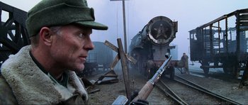 Movie still from “Enemy at the Gates” (2001), directed by Jean-Jacques Annaud – A man with a rifle standing in front of a train; Medium shot, Low angle