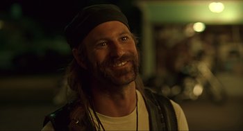 Movie still from “Erin Brockovich” (2000), directed by Steven Soderbergh – A man with long hair and a beard smiling for the camera; Close Up shot, Over the shoulder angle