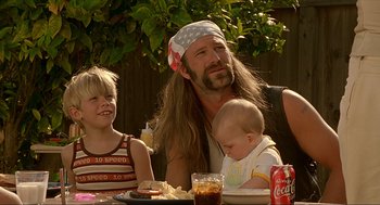 Movie still from “Erin Brockovich” (2000), directed by Steven Soderbergh – A man with long hair and a beard is sitting at a table with a child and an adult; Medium shot, Over the shoulder angle