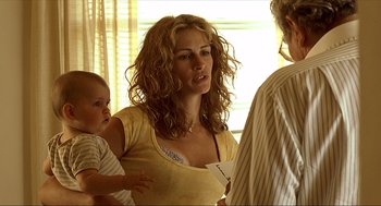 Movie still from “Erin Brockovich” (2000), directed by Steven Soderbergh – A woman holding a paper airplane while holding a baby; Medium shot, Over the shoulder angle
