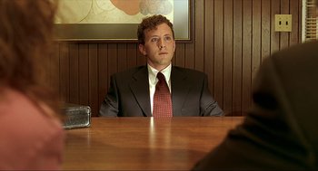 Movie still from “Erin Brockovich” (2000), directed by Steven Soderbergh – A man sitting at a table in front of a picture; Medium shot, Over the shoulder angle