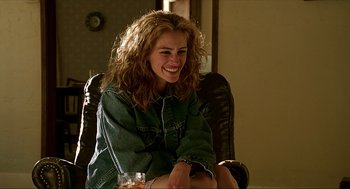 Movie still from “Erin Brockovich” (2000), directed by Steven Soderbergh – A woman sitting in a chair smiling at the camera; Medium shot, Over the shoulder angle