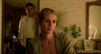 Movie still from “Erin Brockovich” (2000), directed by Steven Soderbergh – A young woman is looking at the camera while a young man stands in the background; Medium shot, Over the shoulder angle