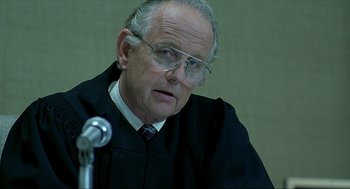 Movie still from “Erin Brockovich” (2000), directed by Steven Soderbergh – An older man wearing a black robe and glasses; Close Up shot, Over the shoulder angle