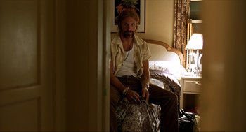 Movie still from “Erin Brockovich” (2000), directed by Steven Soderbergh – A man sitting on a bed holding a cell phone; Medium shot, Low angle