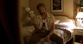 Movie still from “Erin Brockovich” (2000), directed by Steven Soderbergh – A man sitting on top of a bed holding a bottle; Medium shot, Low angle