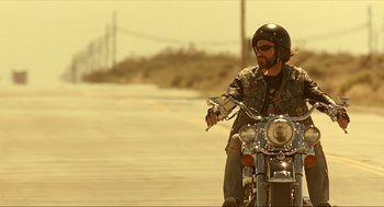 Movie still from “Erin Brockovich” (2000), directed by Steven Soderbergh – A man riding a motorcycle down the middle of a road; Medium shot, Low angle