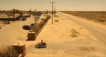 Movie still from “Erin Brockovich” (2000), directed by Steven Soderbergh – A man riding a motorcycle down the middle of a road; Extreme Wide shot, High angle
