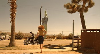Movie still from “Erin Brockovich” (2000), directed by Steven Soderbergh – A woman standing on the side of a road next to a man on a motorcycle; Wide shot, Low angle