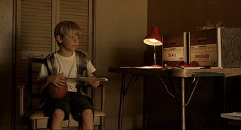 Movie still from “Erin Brockovich” (2000), directed by Steven Soderbergh – A young boy sitting in a chair holding a basketball; Medium shot, High angle