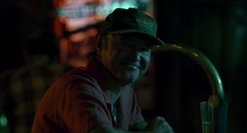 Movie still from “Erin Brockovich” (2000), directed by Steven Soderbergh – An older man wearing a baseball hat and smiling for the camera; Close Up shot, Over the shoulder angle