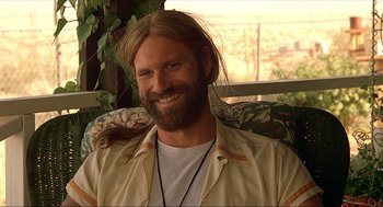Movie still from “Erin Brockovich” (2000), directed by Steven Soderbergh – A man with long hair and a beard smiling for the camera; Close Up shot, Low angle