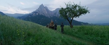 Movie still from “A Hidden Life” (2019), directed by Terrence Malick – A group of people walking in a grassy area with mountains in the background; Extreme Wide shot, Low angle