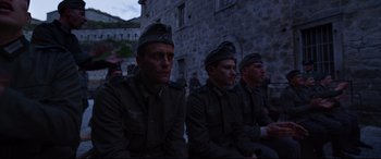 Movie still from “A Hidden Life” (2019), directed by Terrence Malick – A group of men in uniform sitting next to each other in front of a stone building; Medium shot, Low angle