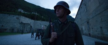 Movie still from “A Hidden Life” (2019), directed by Terrence Malick – A man wearing a helmet and holding a rifle; Medium shot, Over the shoulder angle