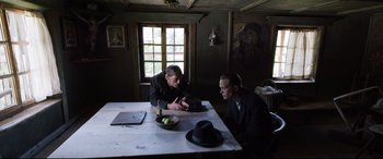 Movie still from “A Hidden Life” (2019), directed by Terrence Malick – Two men sitting at a table in a dark room; Wide shot, Over the shoulder angle