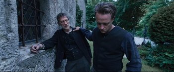 Movie still from “A Hidden Life” (2019), directed by Terrence Malick – Two men standing next to each other near a tree; Medium shot, Over the shoulder angle