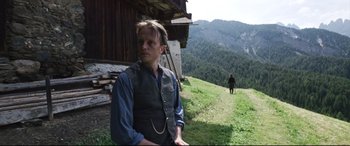 Movie still from “A Hidden Life” (2019), directed by Terrence Malick – A man standing on top of a grass covered hillside; Medium shot, Over the shoulder angle