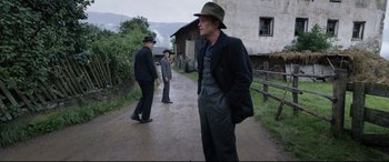 Movie still from “A Hidden Life” (2019), directed by Terrence Malick – A man in a hat is standing on the side of the road; Medium shot, Over the shoulder angle