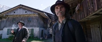 Movie still from “A Hidden Life” (2019), directed by Terrence Malick – A man in a hat and a vest standing in front of a house; Medium shot, Low angle