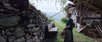 Movie still from “A Hidden Life” (2019), directed by Terrence Malick – A woman standing in front of a stone wall; Wide shot, Low angle
