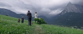 Movie still from “A Hidden Life” (2019), directed by Terrence Malick – A man and a dog are walking on a grassy hill; Extreme Wide shot, Low angle