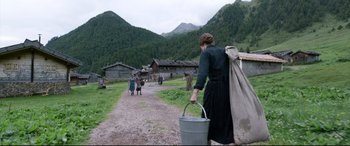 Movie still from “A Hidden Life” (2019), directed by Terrence Malick – A woman holding a bucket walking down a dirt road; Wide shot, High angle