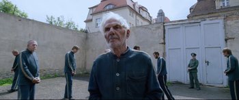 Movie still from “A Hidden Life” (2019), directed by Terrence Malick – An older man standing in front of a brick wall; Medium shot, Over the shoulder angle