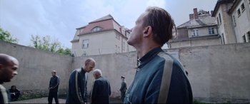Movie still from “A Hidden Life” (2019), directed by Terrence Malick – A group of men standing next to each other in front of a building; Medium shot, Over the shoulder angle