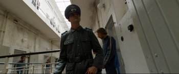 Movie still from “A Hidden Life” (2019), directed by Terrence Malick – A man in a uniform standing next to another man in a building; Medium shot, Low angle