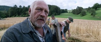 Movie still from “A Hidden Life” (2019), directed by Terrence Malick – An old man with a beard and a hat is in a field with other old men; Close Up shot, Low angle