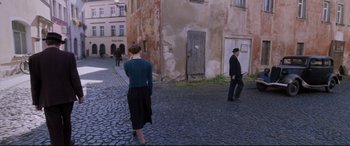 Movie still from “A Hidden Life” (2019), directed by Terrence Malick – A woman walking down a street with a man in a suit; Wide shot, High angle
