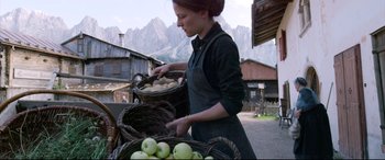 Movie still from “A Hidden Life” (2019), directed by Terrence Malick – A woman holding a basket of apples in front of mountains; Wide shot, Low angle
