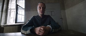 Movie still from “A Hidden Life” (2019), directed by Terrence Malick – A man sitting at a table with his hands crossed; Medium shot, Low angle