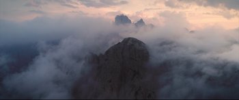 Movie still from “A Hidden Life” (2019), directed by Terrence Malick – A view of a mountain in the middle of a cloud filled sky at sunset; Extreme Wide shot, High angle