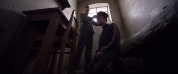 Movie still from “A Hidden Life” (2019), directed by Terrence Malick – A man sitting on the ground with another man standing next to him; Medium shot, Low angle