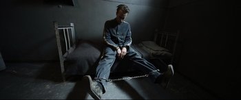 Movie still from “A Hidden Life” (2019), directed by Terrence Malick – A man sitting on a bed chained to a wall; Wide shot, High angle